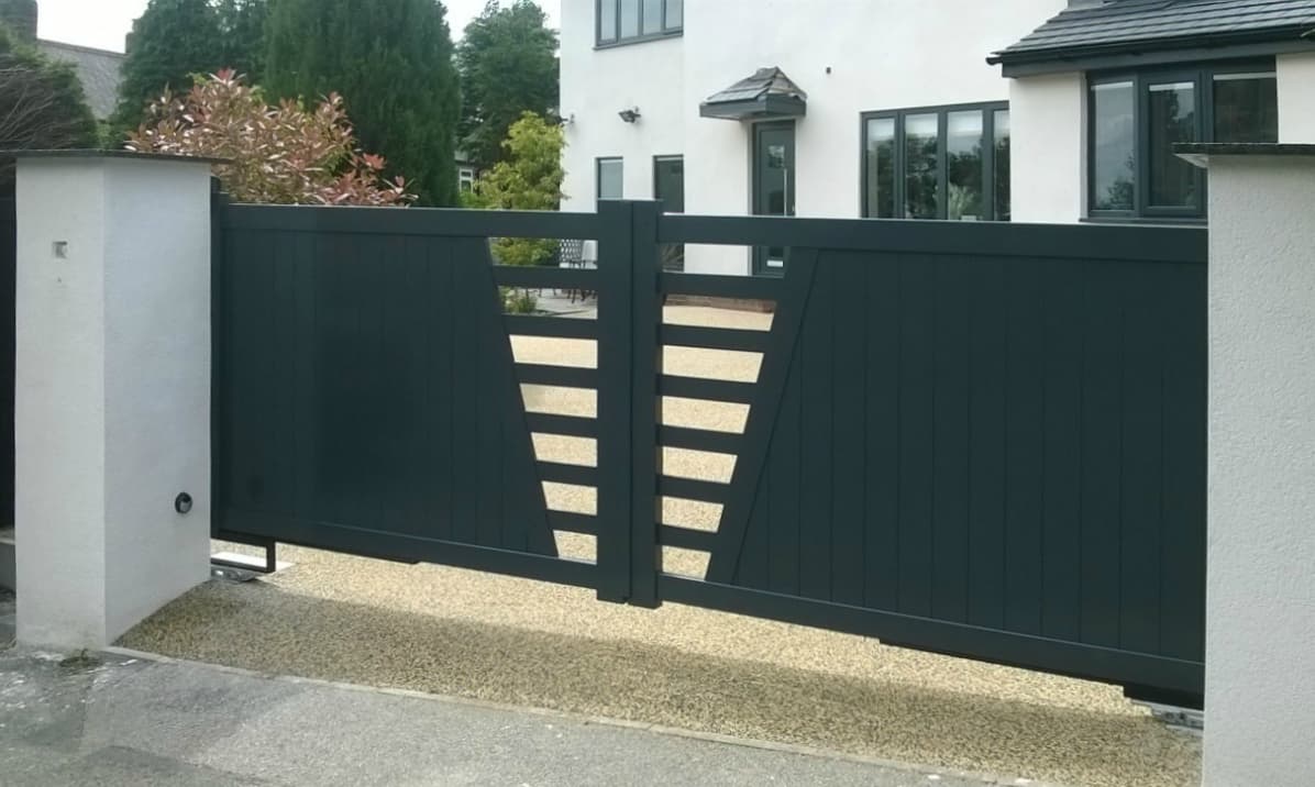 Modern house with a dark grey aluminium gate featuring horizontal cut-out slats, complemented by light-colored walls and greenery.